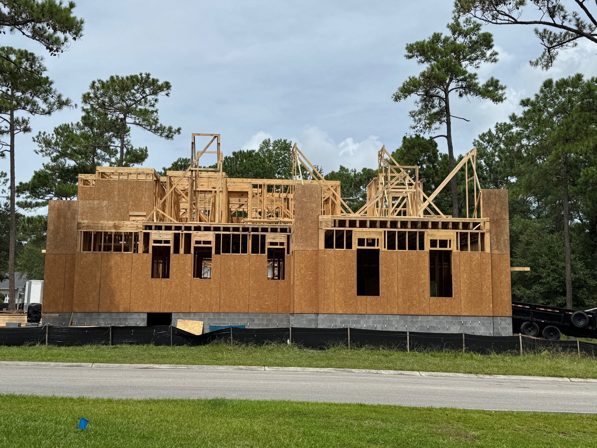 A custom home at the framing stage seen from the street, exterior walls up and roof framing begun.
