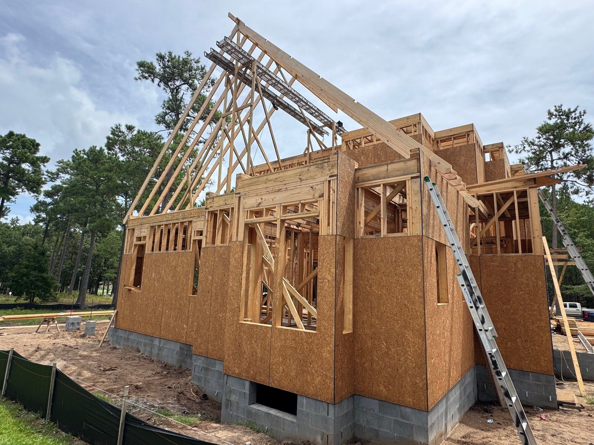 A custom home under construction, roof trusses being raised over the sheathed walls.