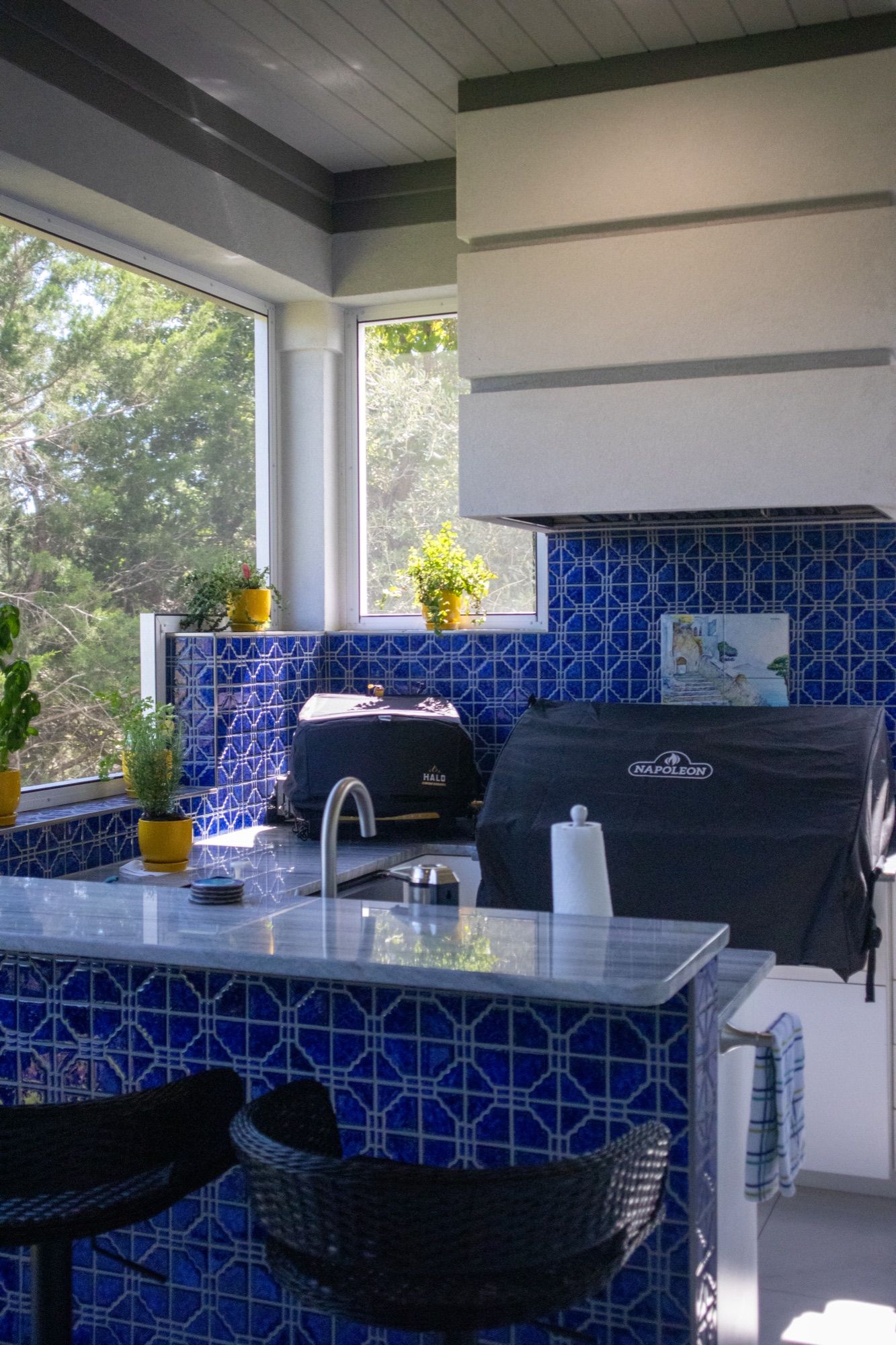 A covered outdoor kitchen with a grill, blue tile, and bar seating.