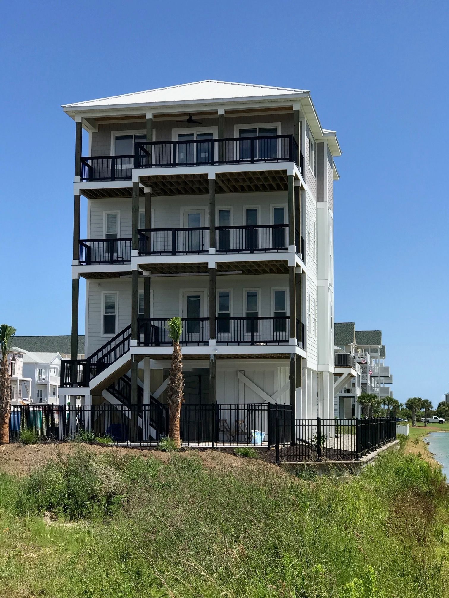 A completed elevated coastal home on pilings, with wraparound porches near the water.